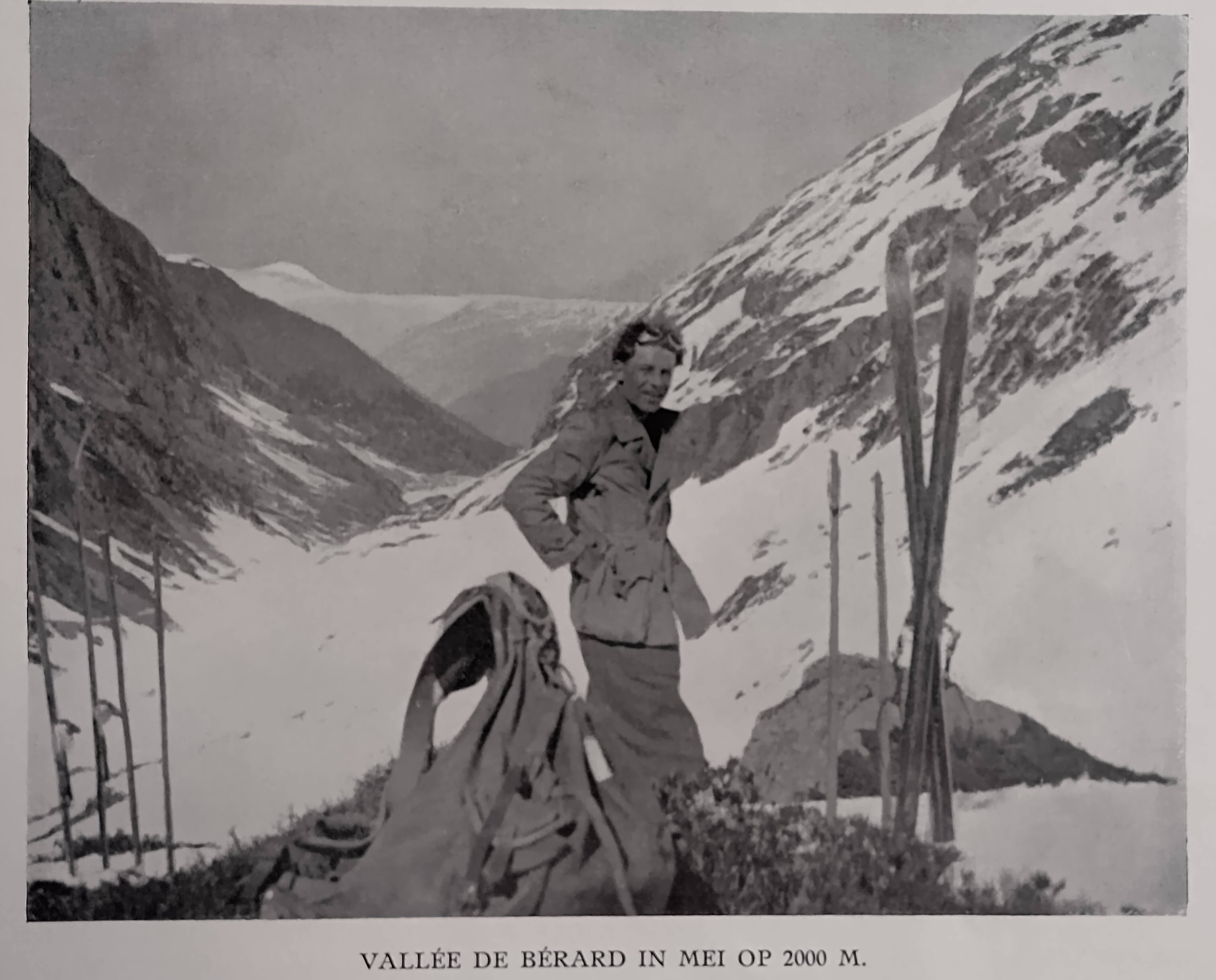 Man met ouderwetse ski-uitrusting, sneeuwbril op het voorhoofd, voor een besneeuwde vallei met links en rechts deels besneeuwde berghellingen. Onderschrift: Vallée de Bérard in mei op 200 m. 